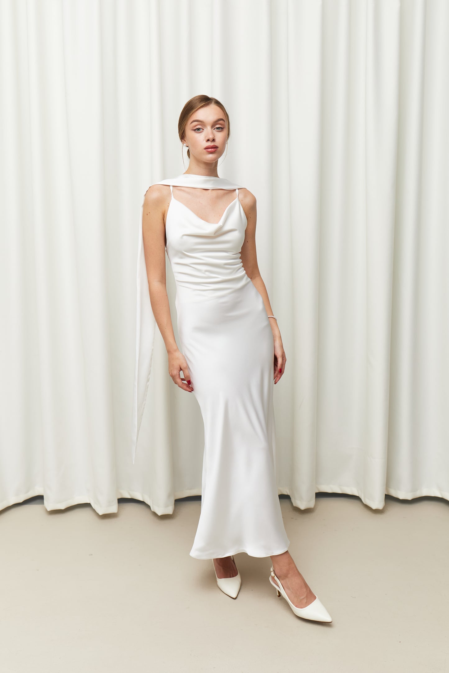 Woman wearing a white dress standing against a white curtain